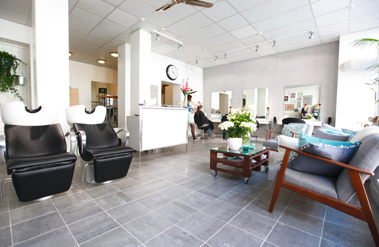 Kampaamo L'Artist sisätilat, Katja leikkaa asiakkaan hiuksia, Enna ja Milla nojaavat seinään