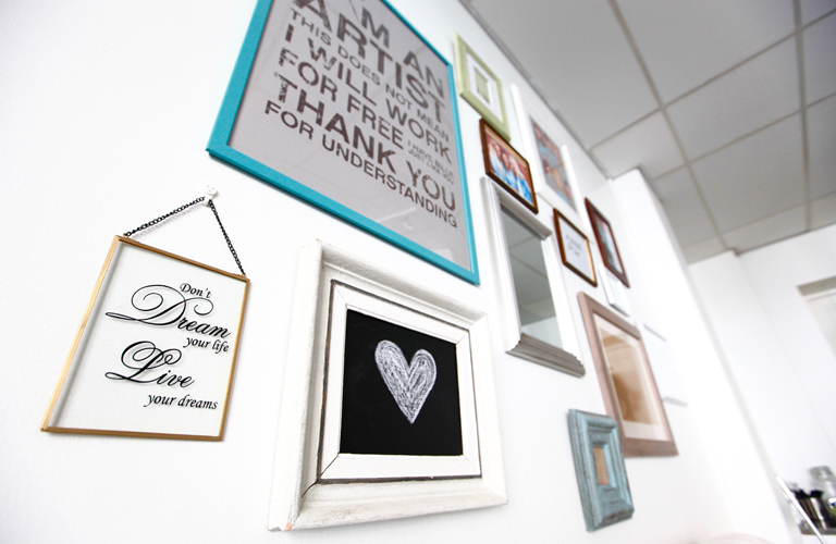 Kampaamo L'Artist seinä, jossa tauluja ja mietelauseita